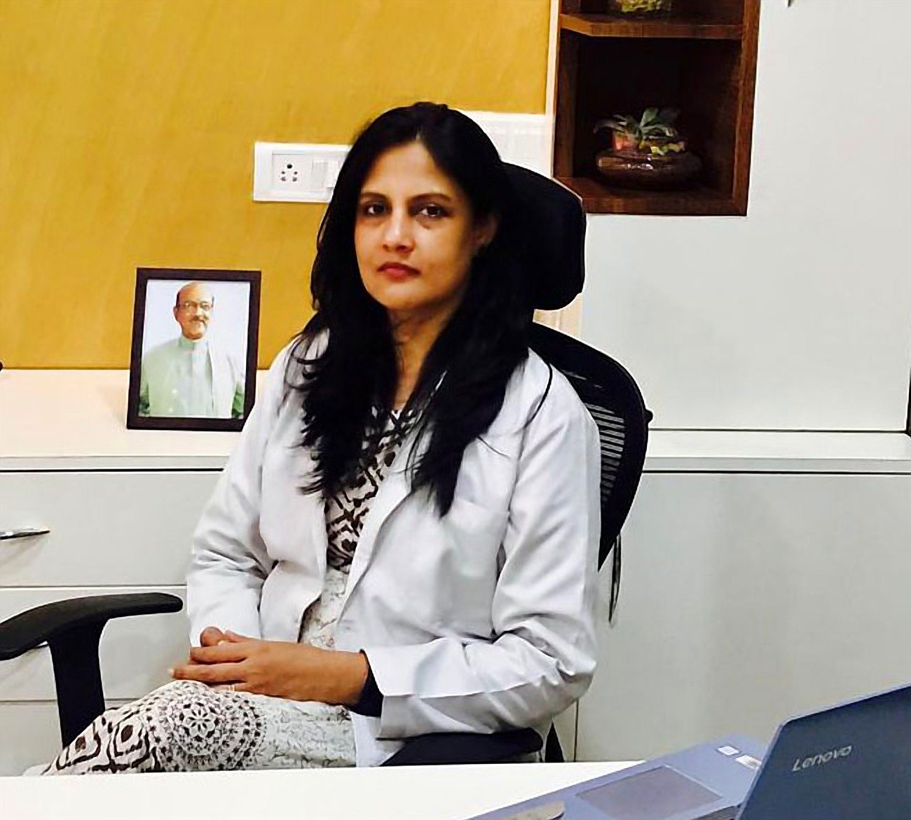 Dr. Rinku Das at her desk, with her father’s portrait on the wall behind her